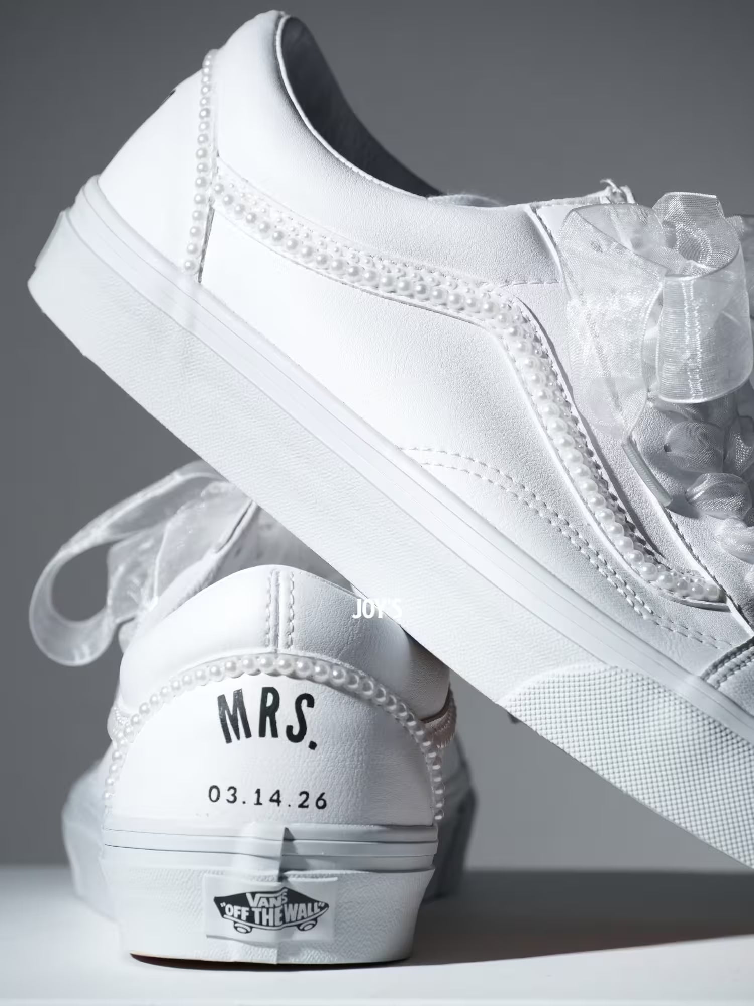 Custom white Vans sneakers with pearl trim and “Mrs.” lettering on the heel, designed as bridal shoes.