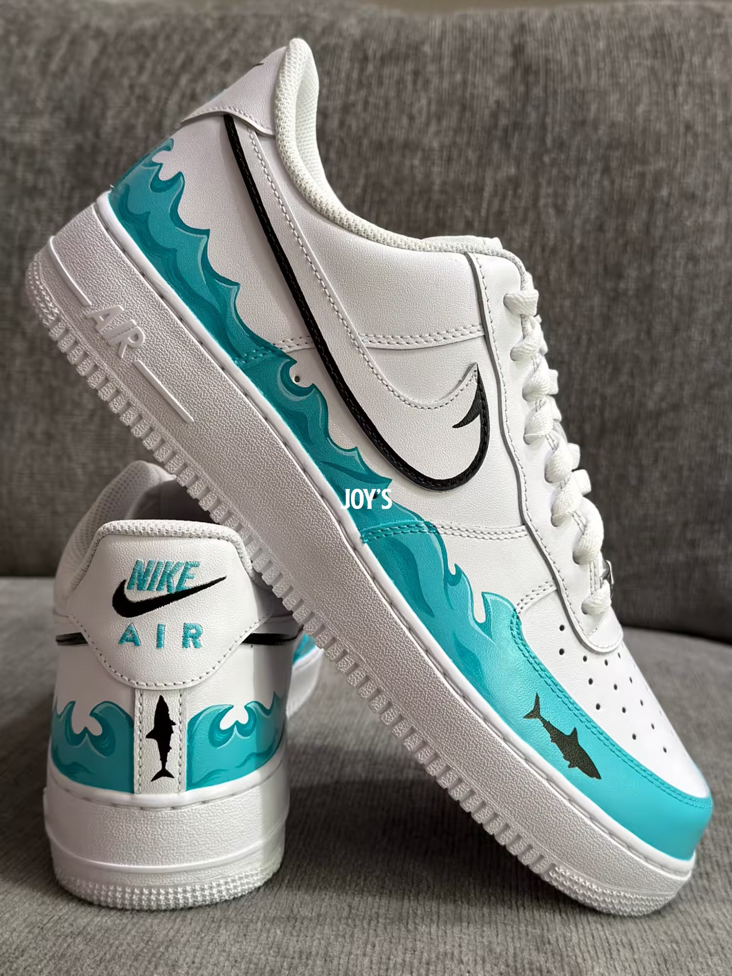 White custom Nike Air Force 1 sneakers with teal sea wave inspired hand-painted details and black swoosh with a shark figure