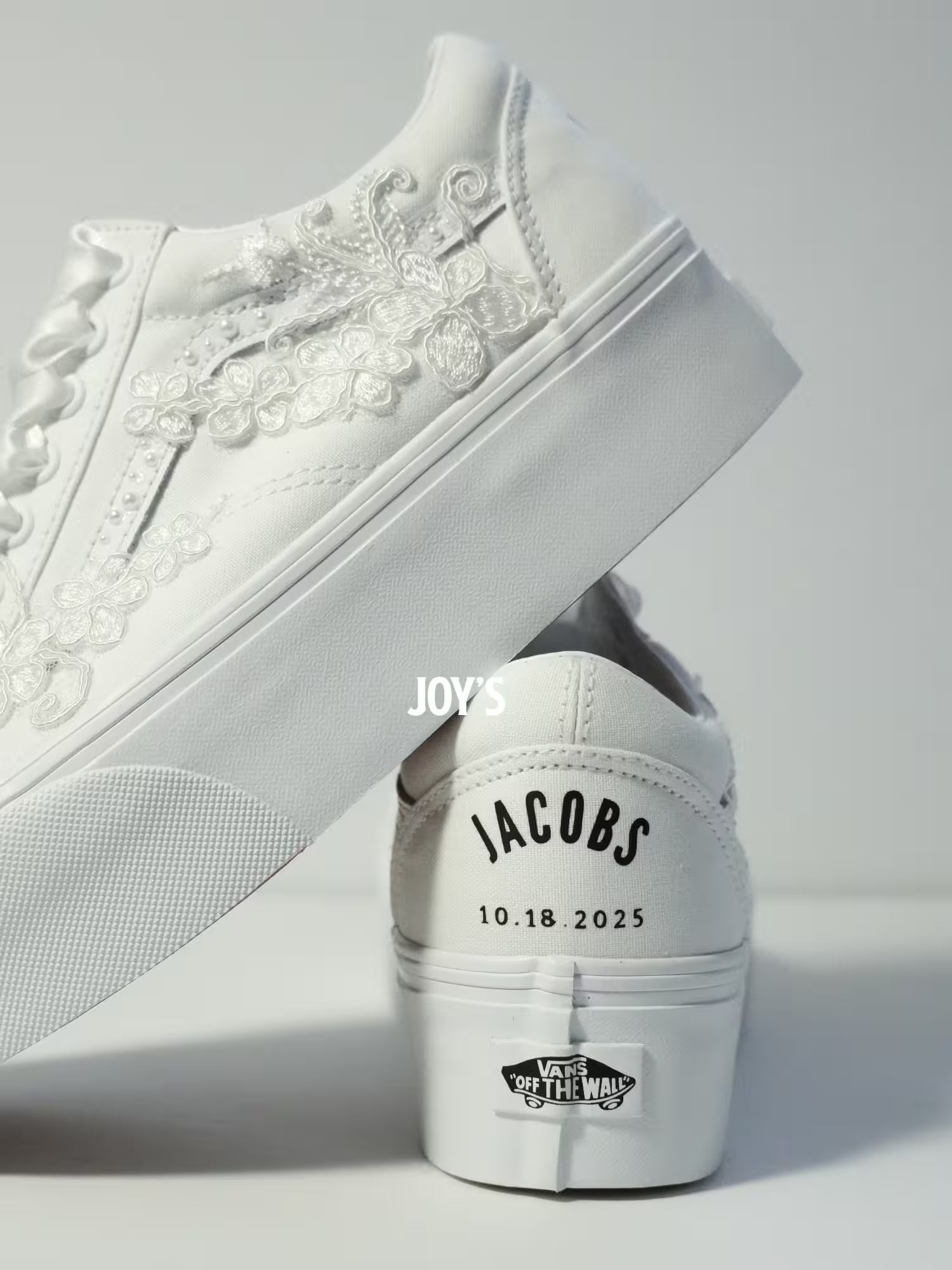 White platform Vans wedding sneakers with lace floral appliqués, pearl detailing, and satin ribbon laces, shown in a close-up side view