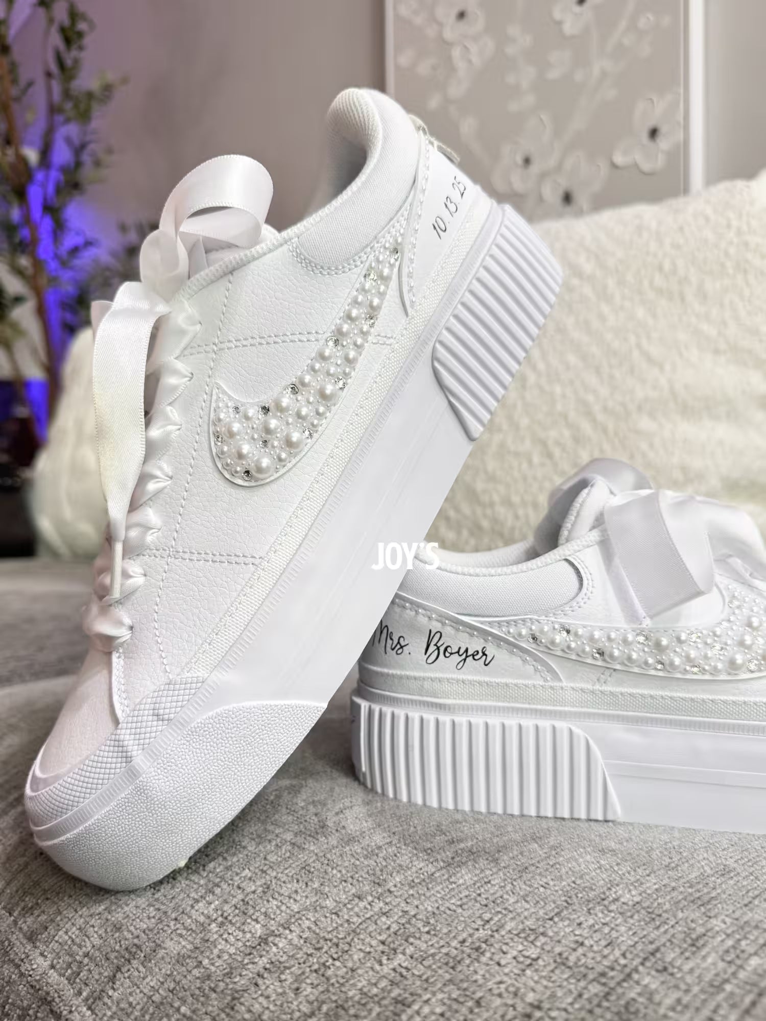 White custom wedding sneakers with pearl and rhinestone embellished swoosh, satin ribbon laces, and personalized bride name and wedding date on the heel