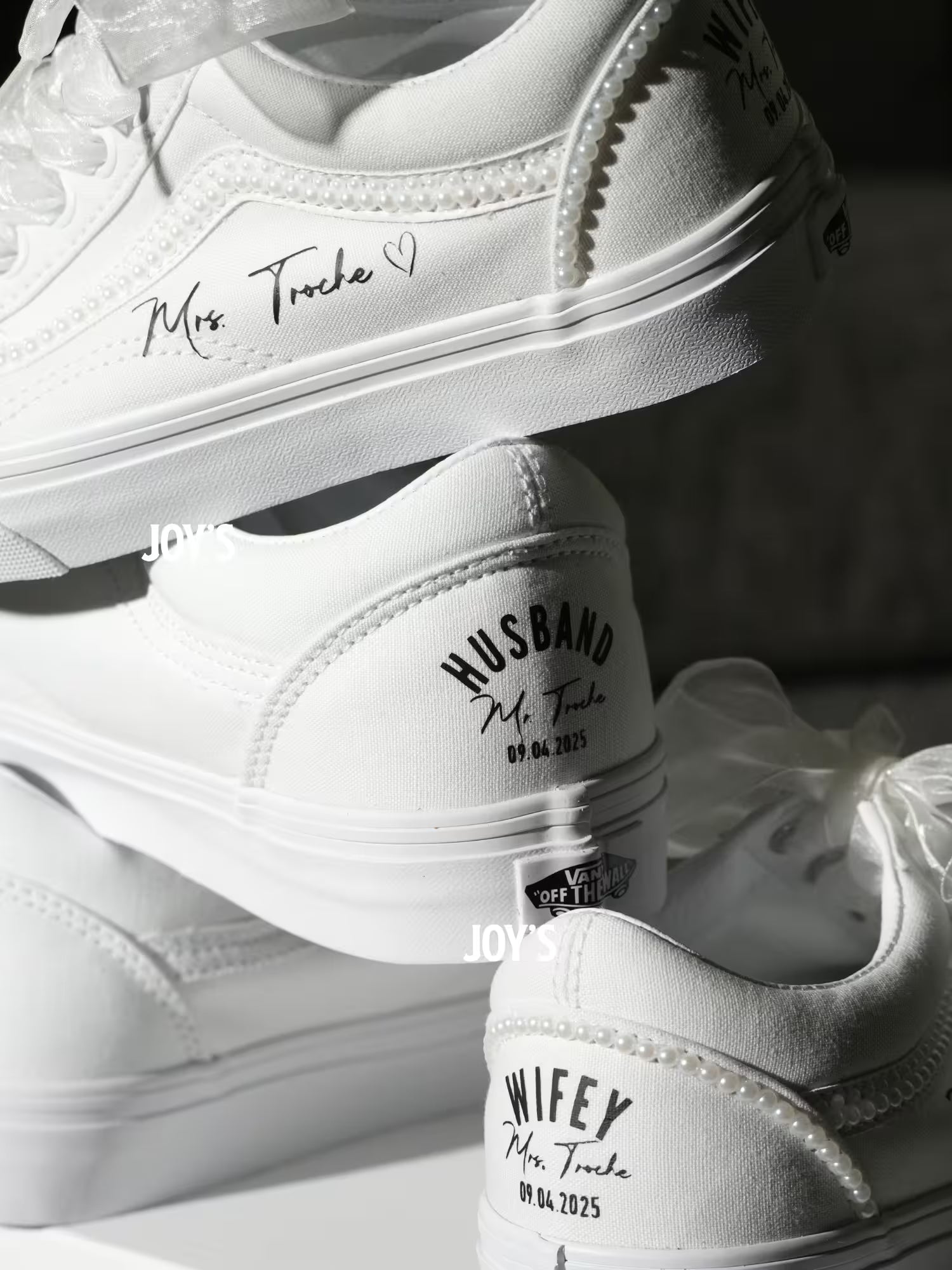 White custom wedding sneakers with pearl trim and personalized bride and groom names, wedding date, and “Wifey” and “Husband” heel text shown in a close-up detail view