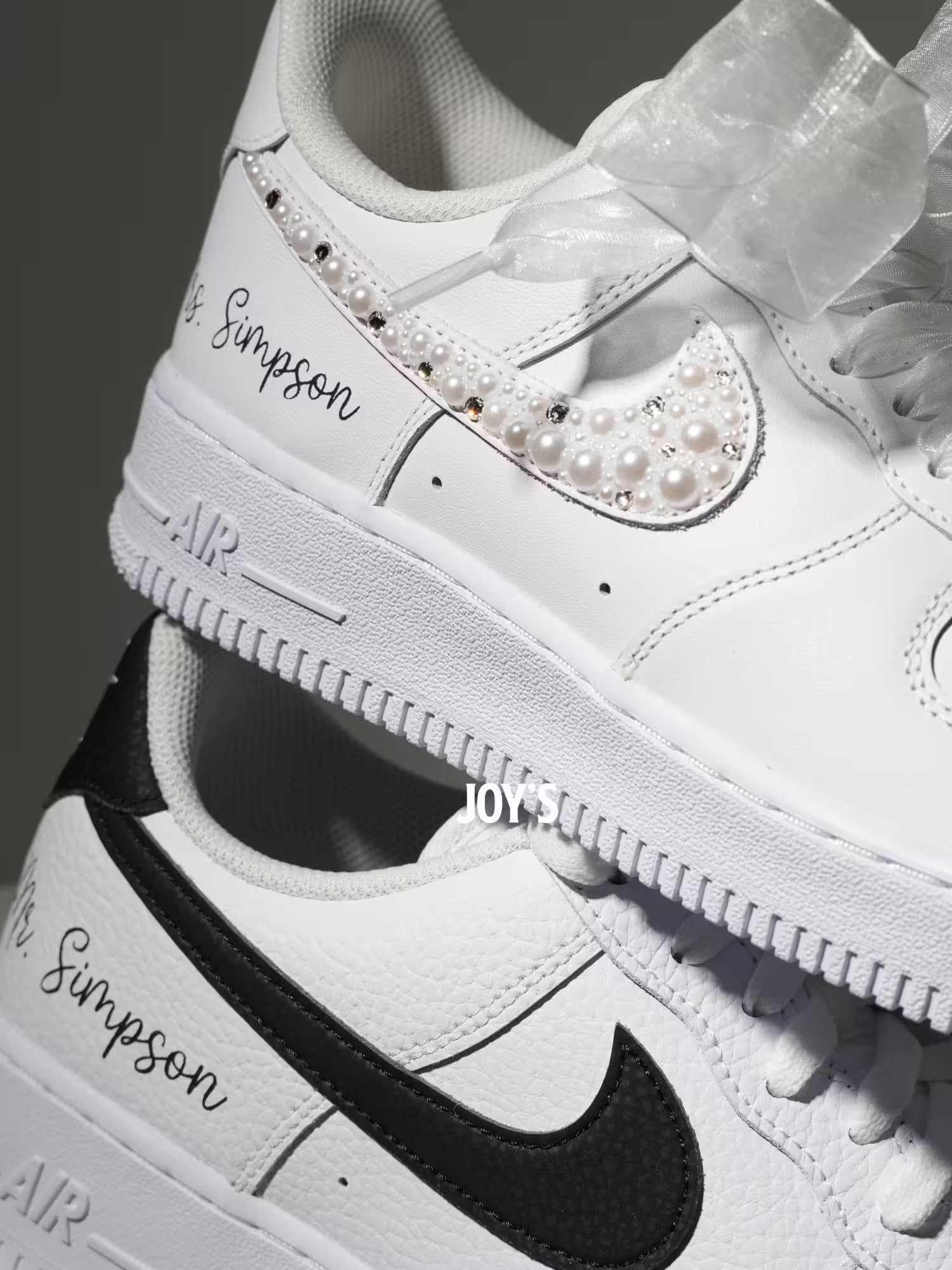 White custom wedding sneakers with pearl and rhinestone embellished swoosh, satin ribbon laces, and personalized last name printed on the side, shown in a close-up detail view