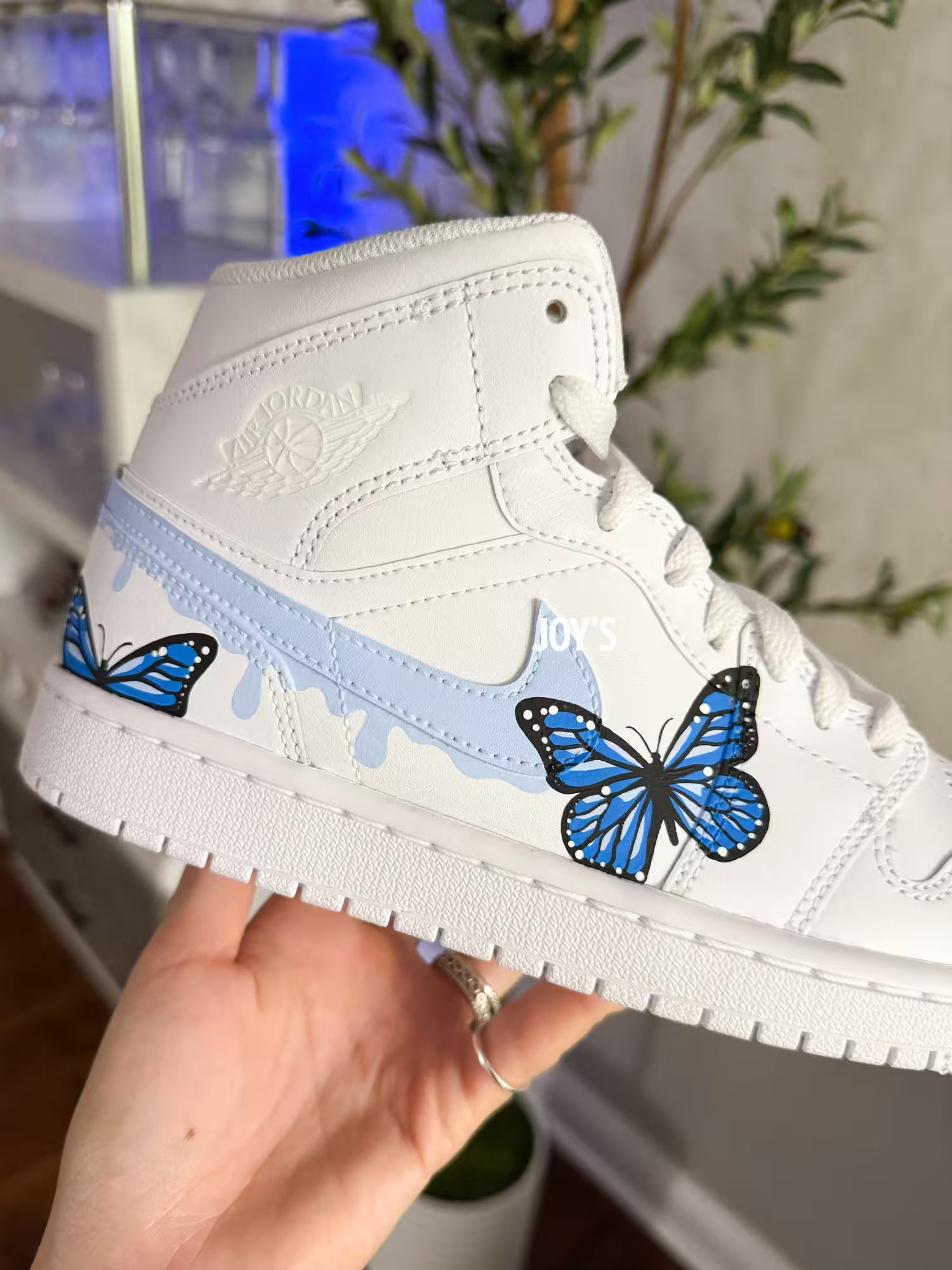 White custom Air Jordan 1 sneakers with hand-painted blue butterfly designs and light blue drip details on the sides, shown in a paired side view