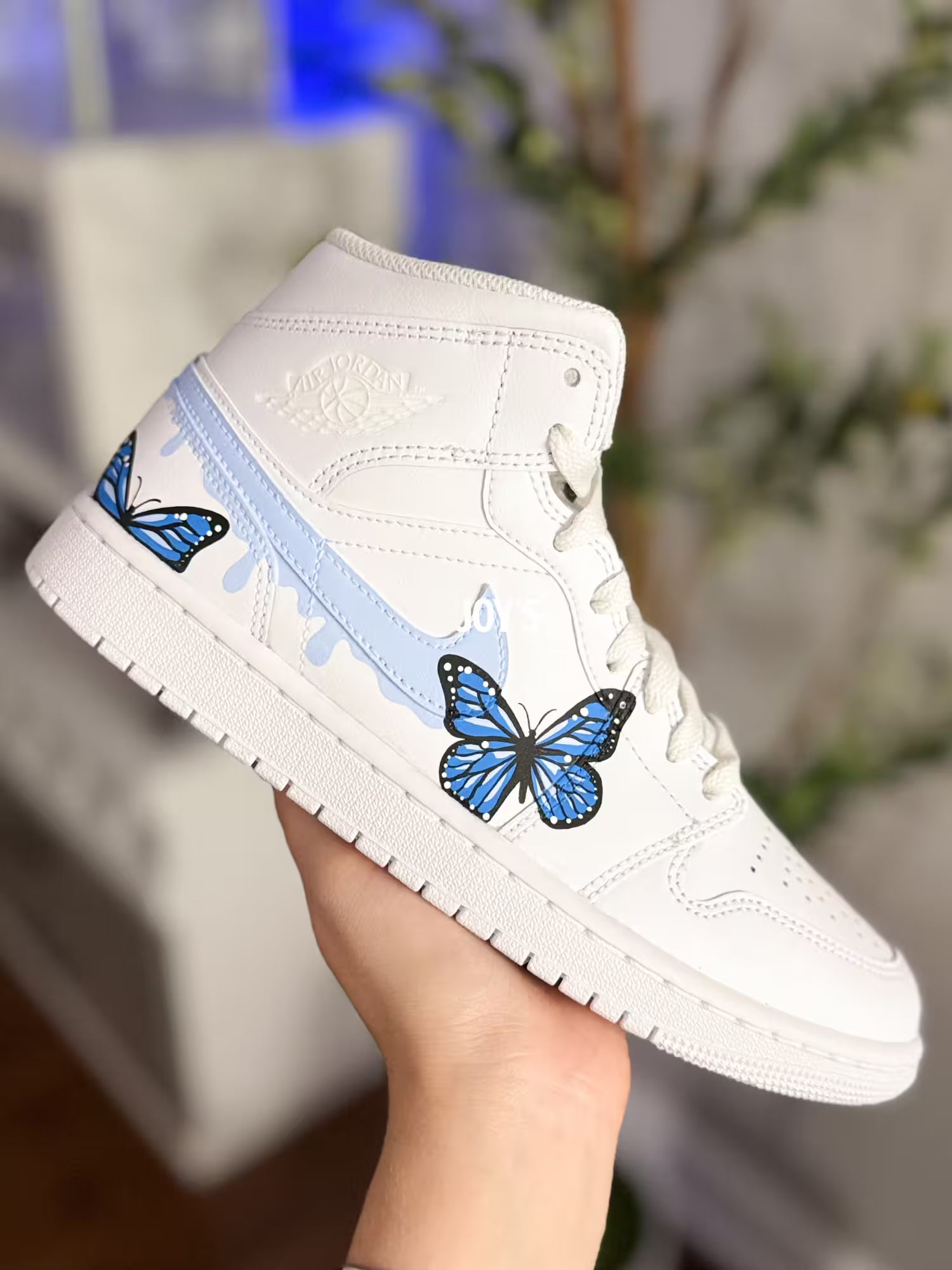 White custom Air Jordan 1 sneakers with hand-painted blue butterfly designs and light blue drip details on the sides, shown in a paired side view
