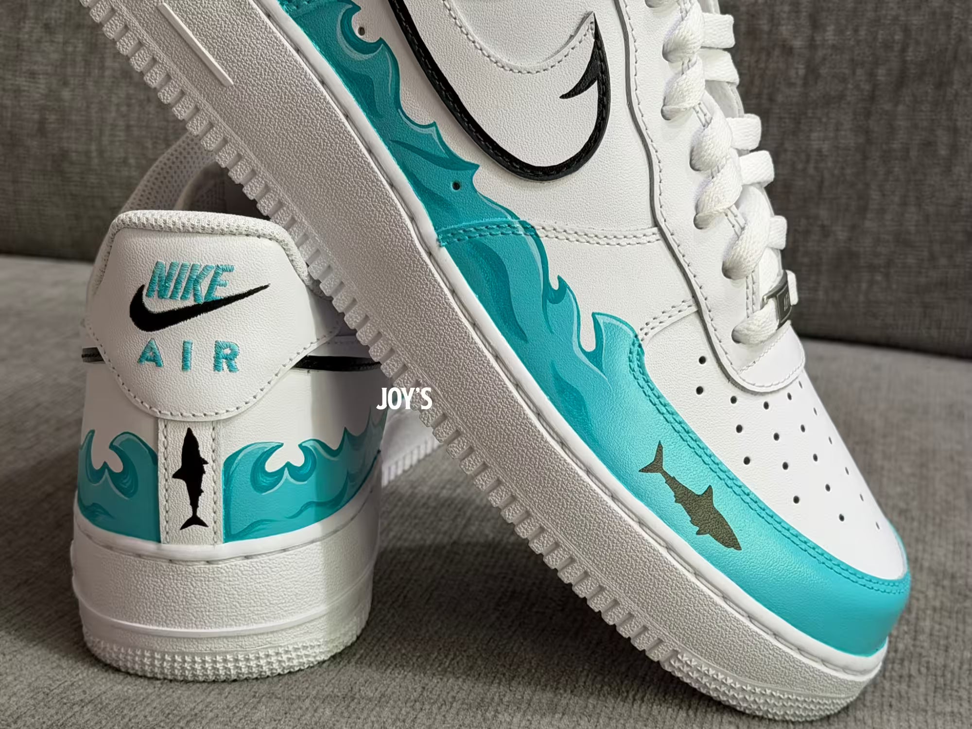 White custom Nike Air Force 1 sneakers with teal sea wave inspired hand-painted details and black swoosh with a shark figure
