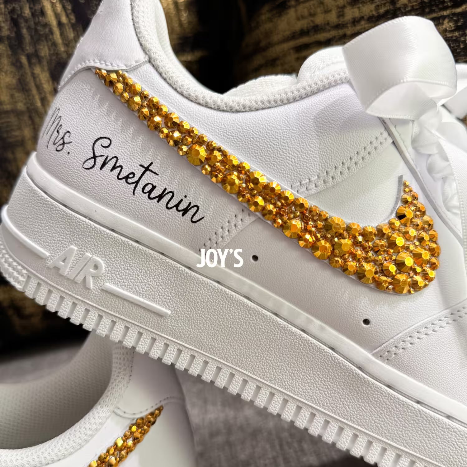 White custom wedding sneakers featuring gold rhinestone swooshes, personalized name and wedding date on the heel, shown in a close-up detail view