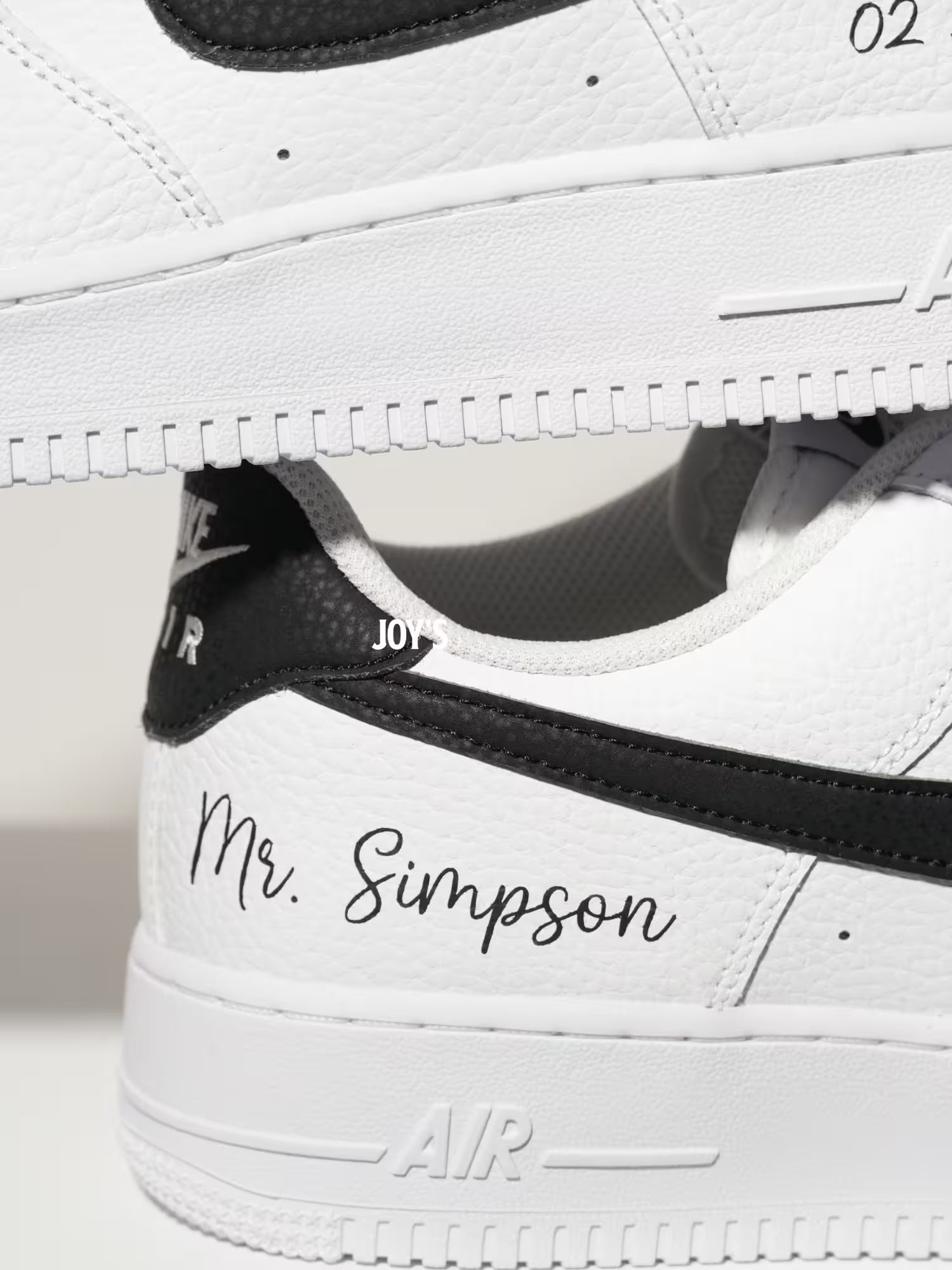 White custom Nike Air Force 1 sneakers with black swoosh, personalized last name and wedding date printed on the side, shown in a clean close-up view