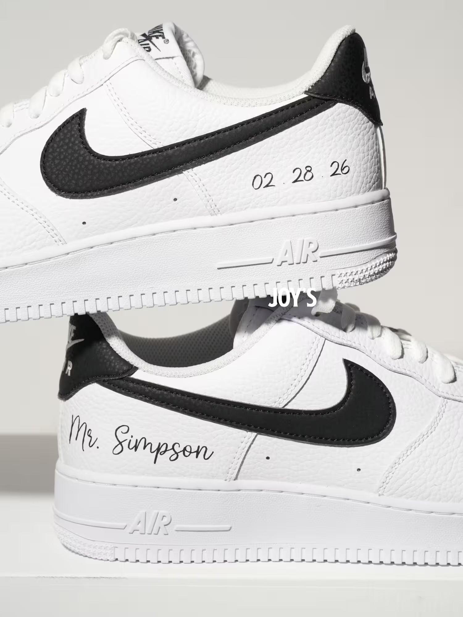 White custom Nike Air Force 1 sneakers with black swoosh, personalized last name and wedding date printed on the side, shown in a clean close-up view