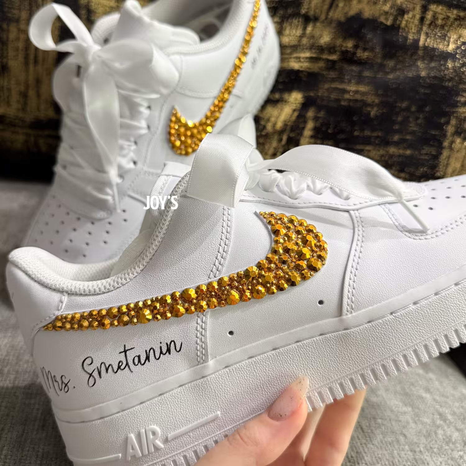 White custom wedding sneakers featuring gold rhinestone swooshes, personalized name and wedding date on the heel, shown in a close-up detail view