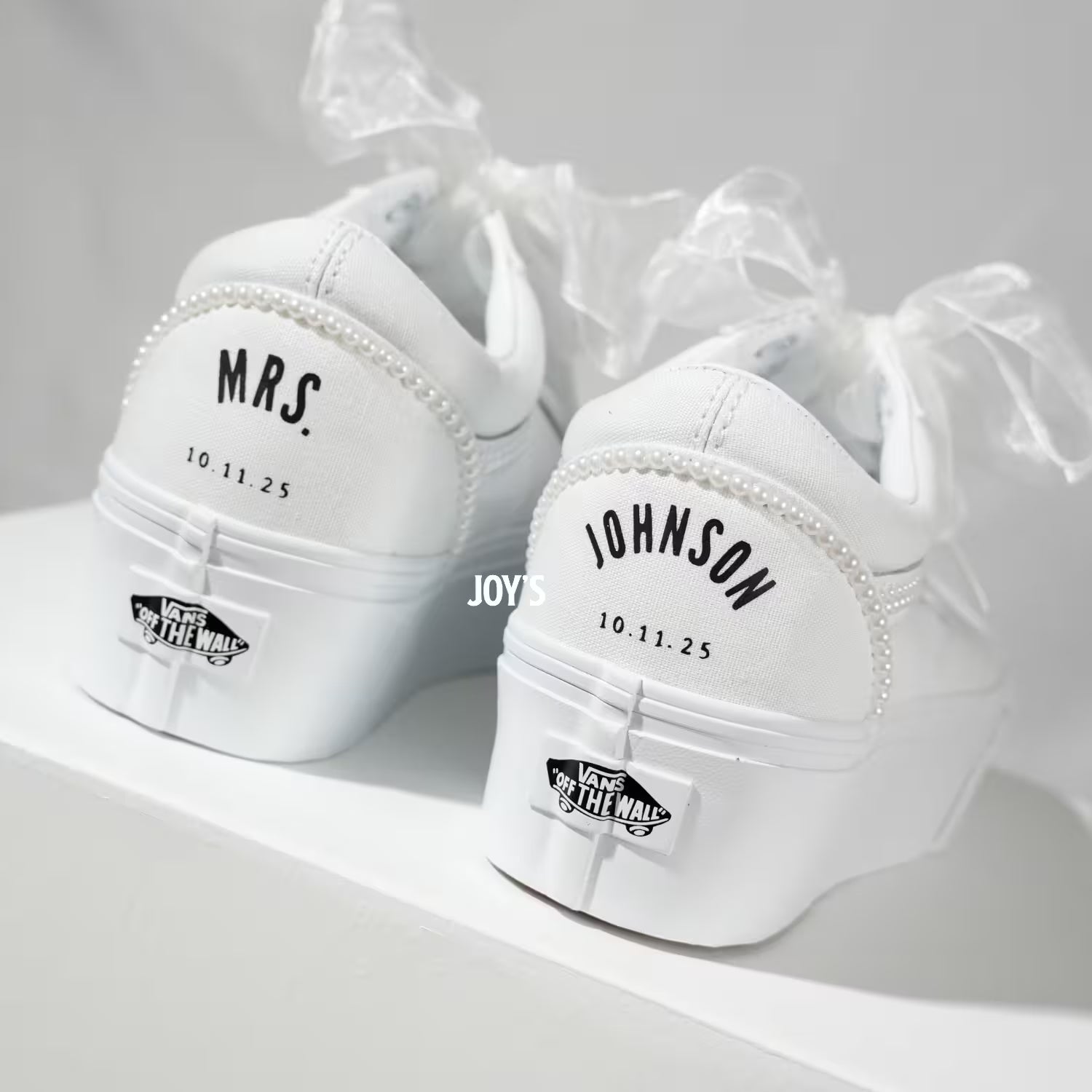White platform Vans wedding sneakers with pearl trim, satin ribbon laces, and personalized “Mrs.” and last name with wedding date printed on the heels, shown in a rear view