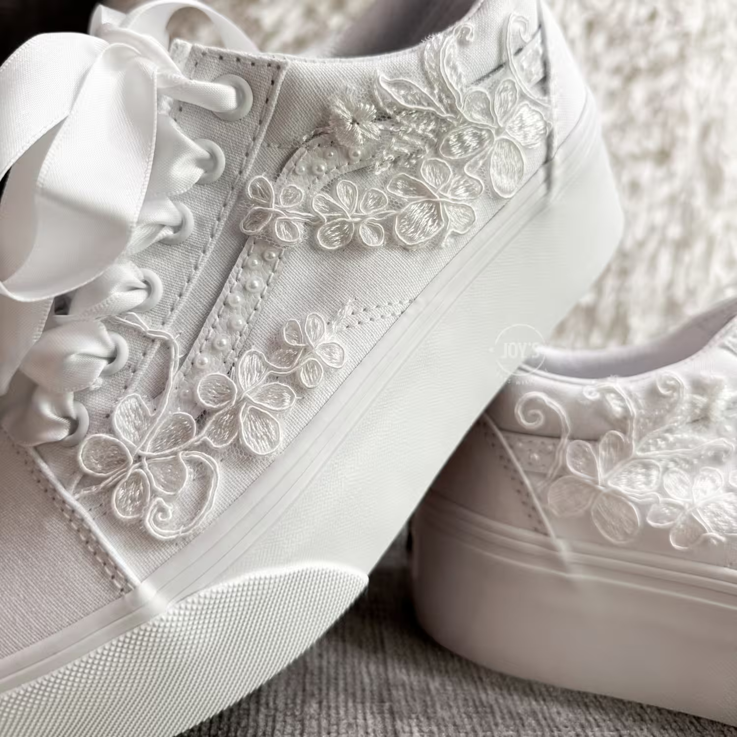 White platform Vans wedding sneakers with lace floral appliqués, pearl detailing, and satin ribbon laces, shown in a close-up side view