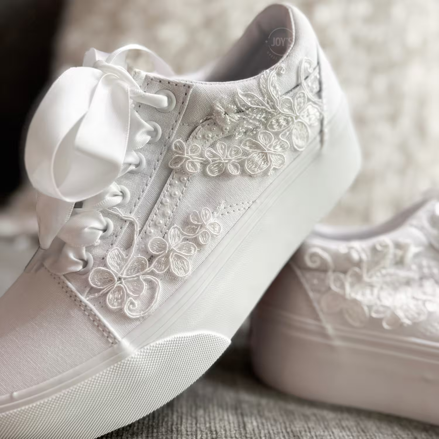 White platform Vans wedding sneakers with lace floral appliqués, pearl detailing, and satin ribbon laces, shown in a close-up side view
