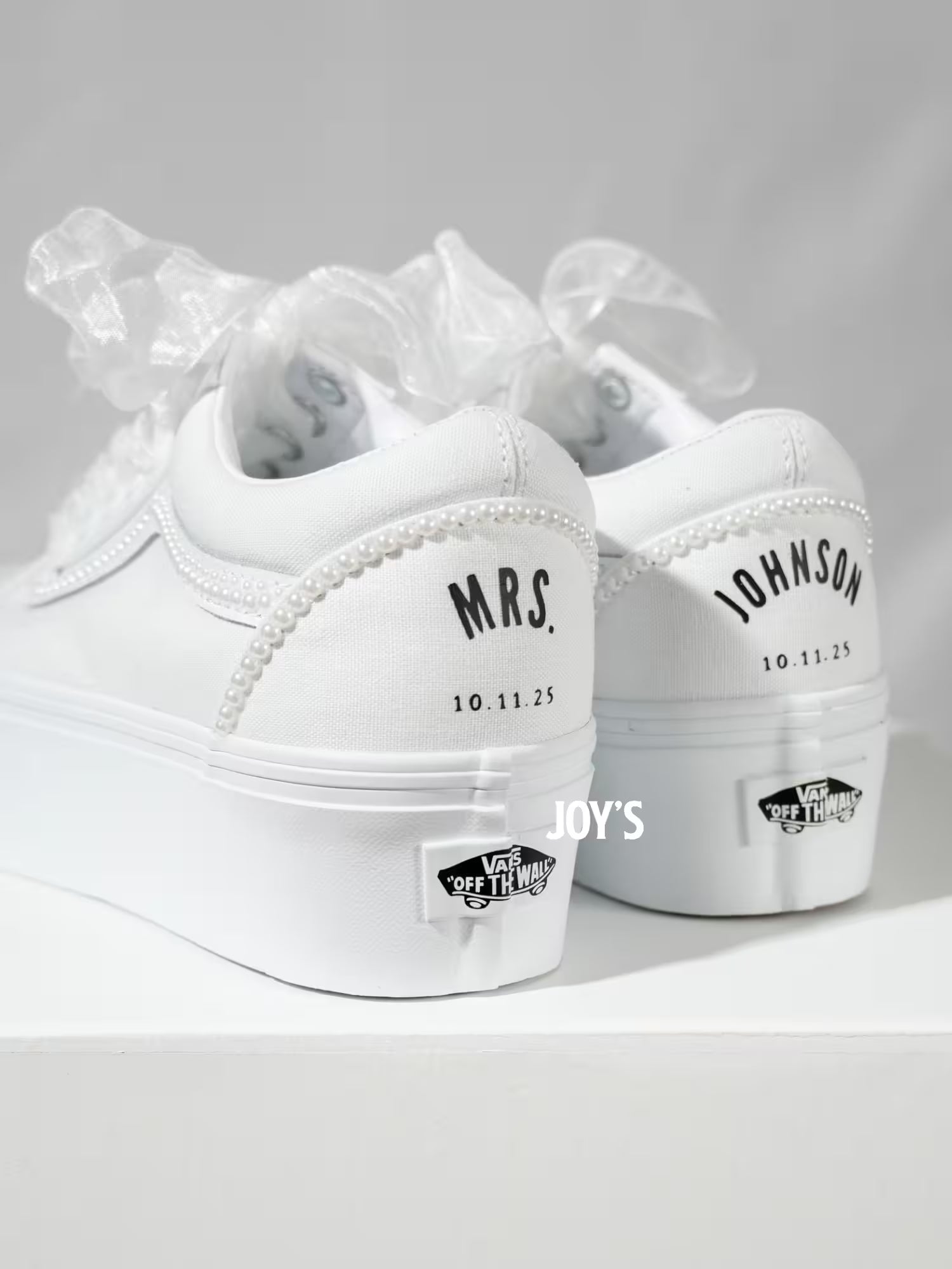 White platform Vans wedding sneakers with pearl trim, satin ribbon laces, and personalized “Mrs.” and last name with wedding date printed on the heels, shown in a rear view