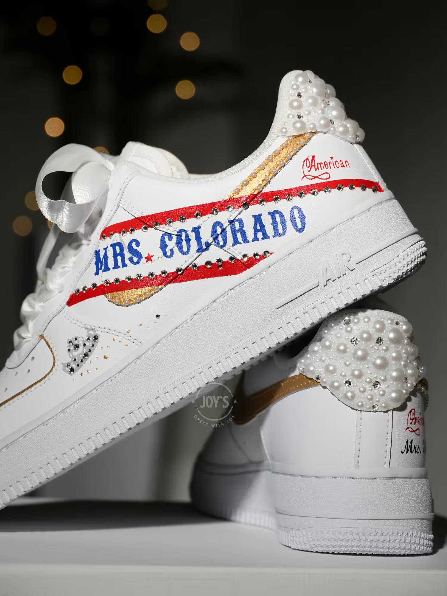 White custom wedding sneakers with pearl-embellished heel, rhinestone details, red and blue painted accents, and personalized “Mrs. Colorado” text on the side, shown in a close-up side view