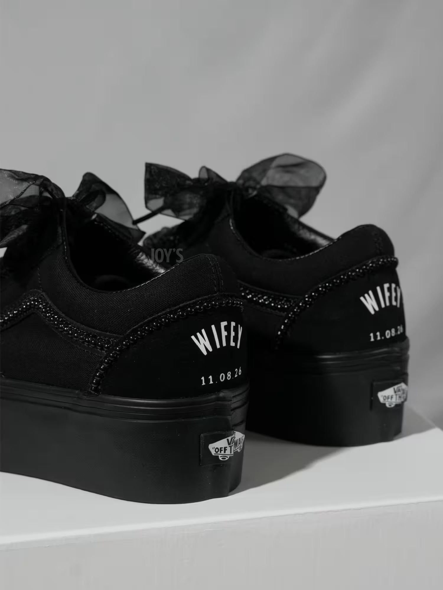 Black platform Vans custom wedding sneakers with pearl trim, satin ribbon laces, and “Wifey” text with wedding date printed on the heel, shown in a close-up rear view