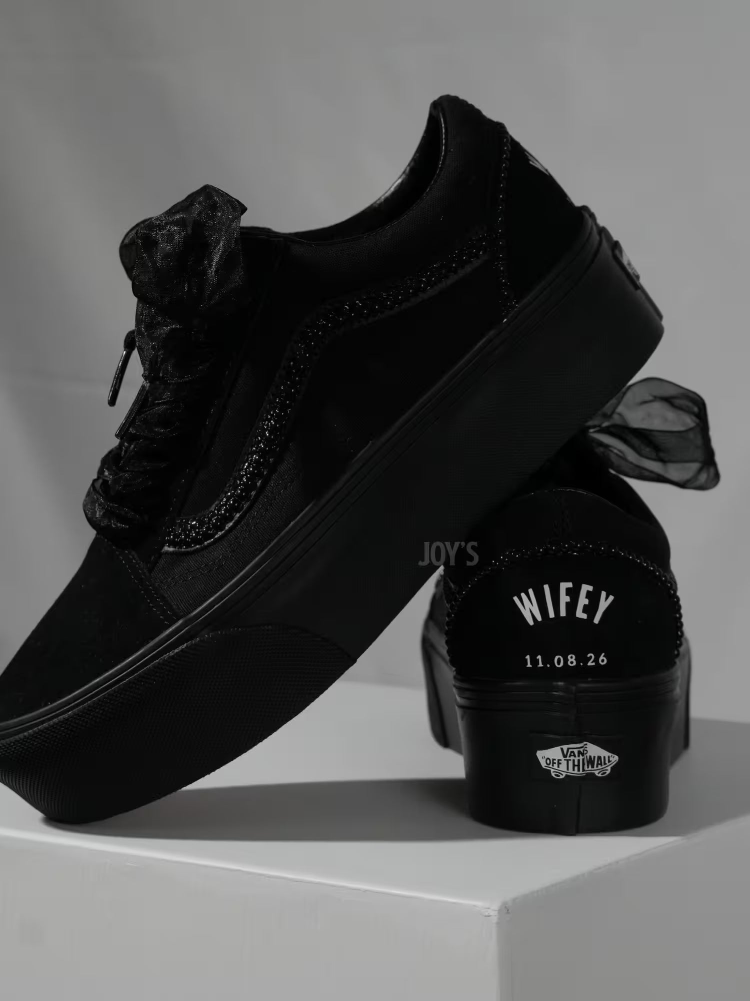 Black platform Vans custom wedding sneakers with pearl trim, satin ribbon laces, and “Wifey” text with wedding date printed on the heel, shown in a close-up rear view
