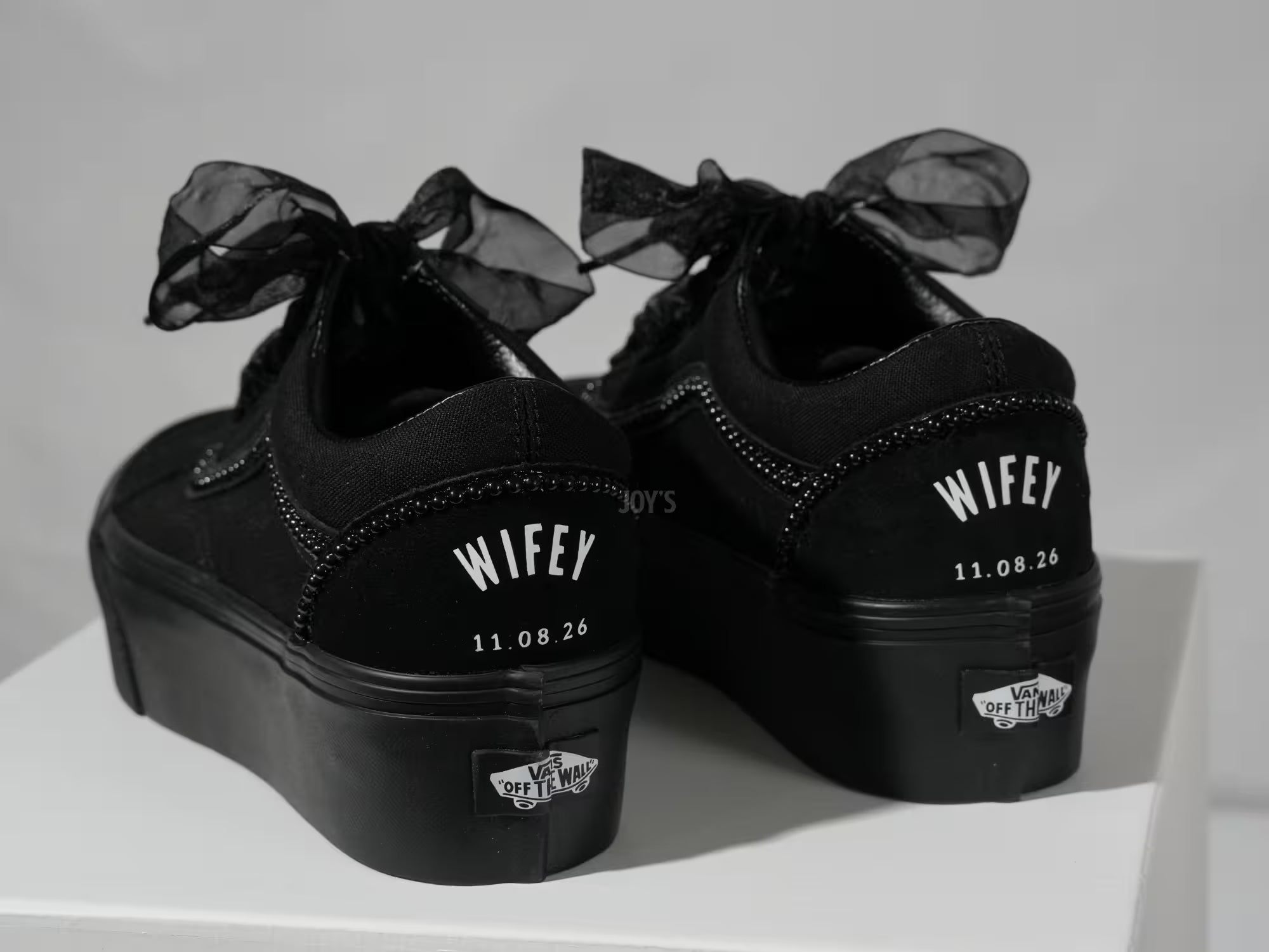 Black platform Vans custom wedding sneakers with pearl trim, satin ribbon laces, and “Wifey” text with wedding date printed on the heel, shown in a close-up rear view