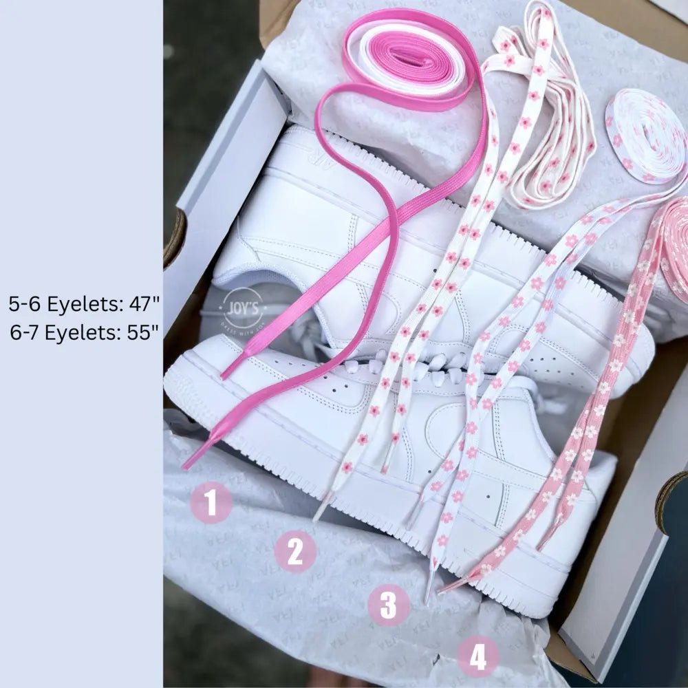 Pink sneaker lace options displayed in a box, including solid pink satin laces and white laces with pink floral patterns, shown rolled and laid out to compare styles and lengths.