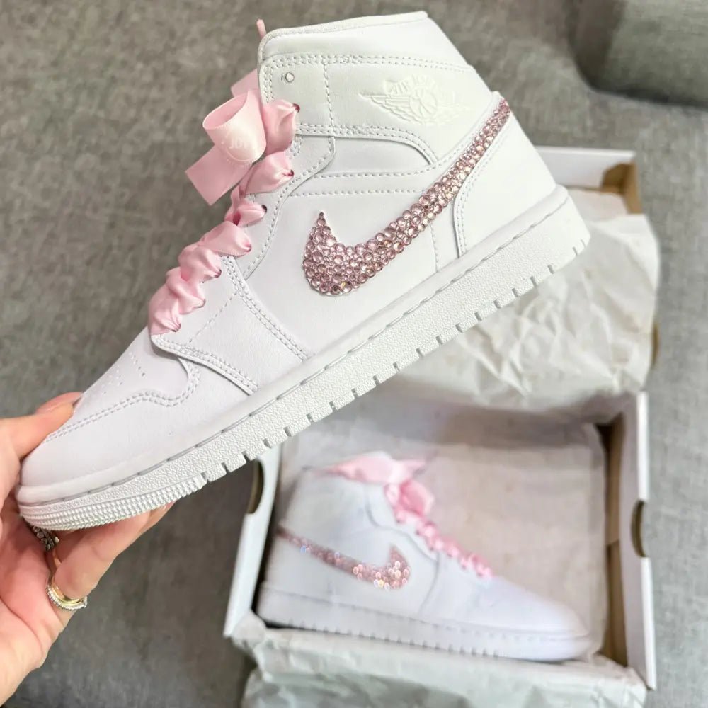White Nike Air Force 1 Mid sneakers (standard sole, not platform), customized with a blush-pink crystal swoosh and matching pink ribbon laces. Clean, elegant finish with a soft bridal vibe, keeping the classic AF1 profile while adding subtle sparkle.