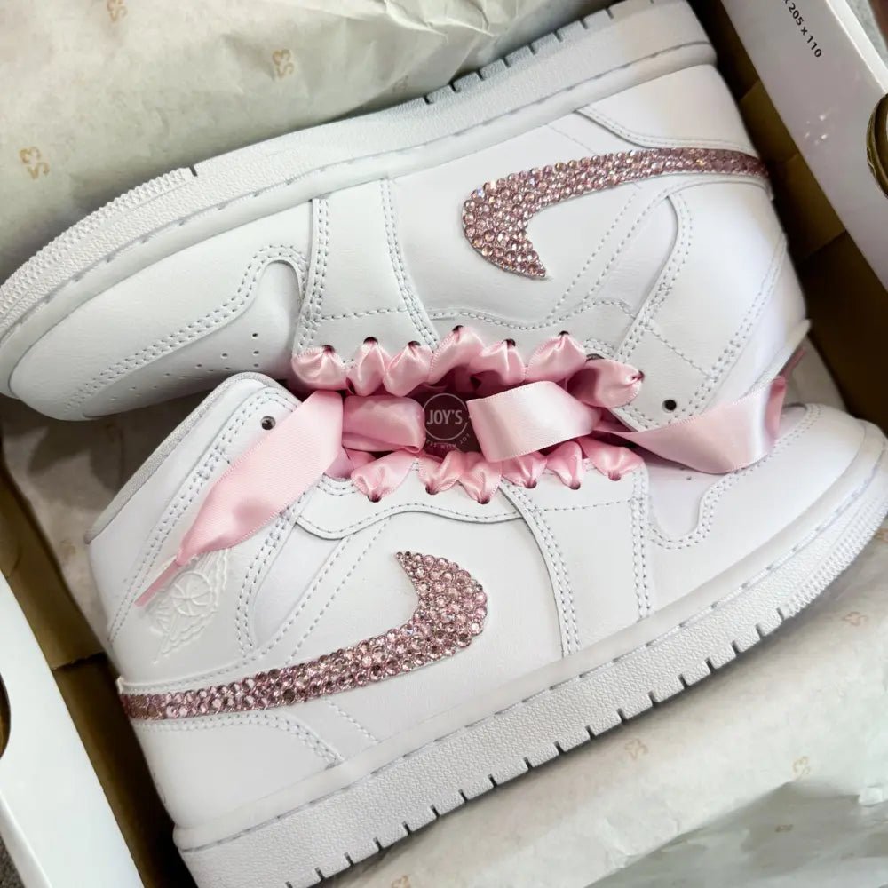 White Nike Air Force 1 Mid sneakers (standard sole, not platform), customized with a blush-pink crystal swoosh and matching pink ribbon laces. Clean, elegant finish with a soft bridal vibe, keeping the classic AF1 profile while adding subtle sparkle.