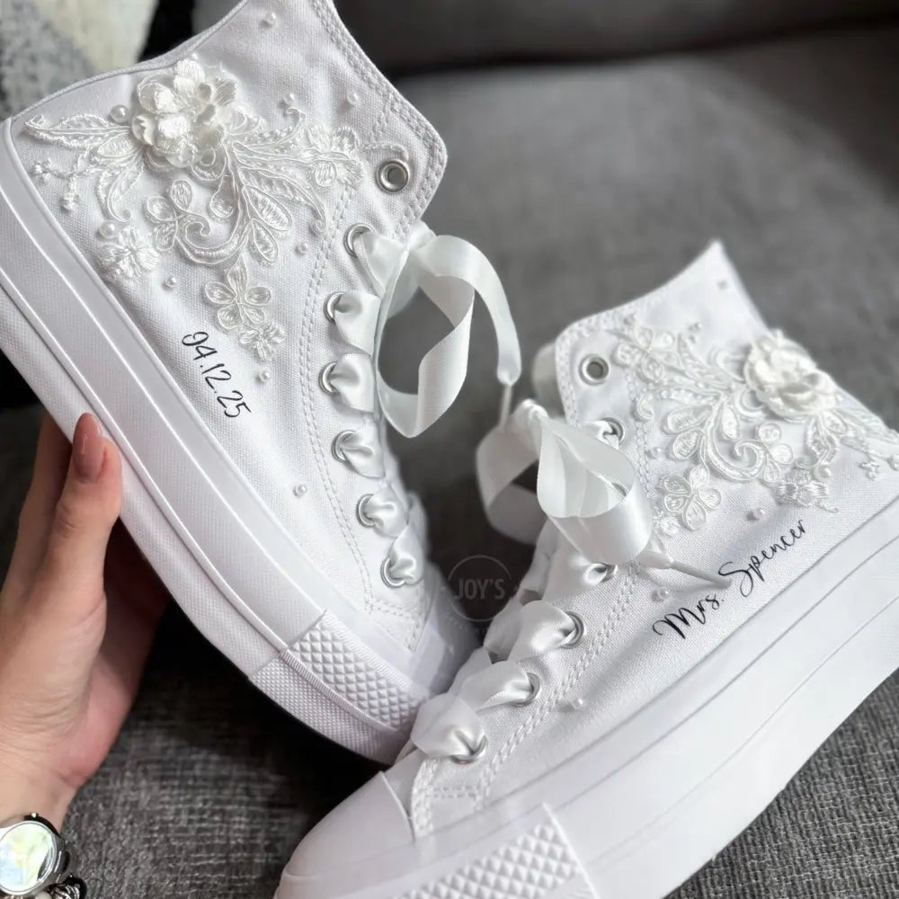 White platform Vans wedding sneakers with lace floral appliqués, satin ribbon laces, and personalized bride name printed on the side, shown in a close-up angled view