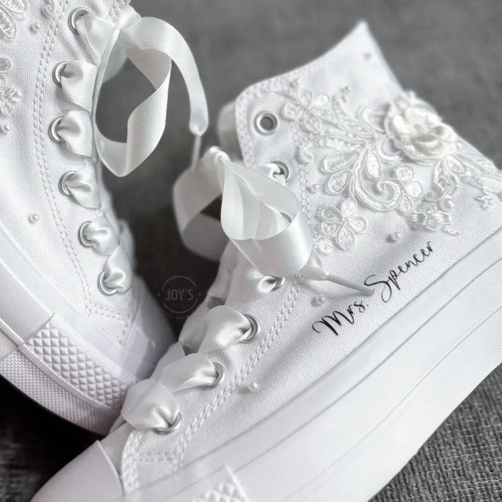 White platform Vans wedding sneakers with lace floral appliqués, satin ribbon laces, and personalized bride name printed on the side, shown in a close-up angled view