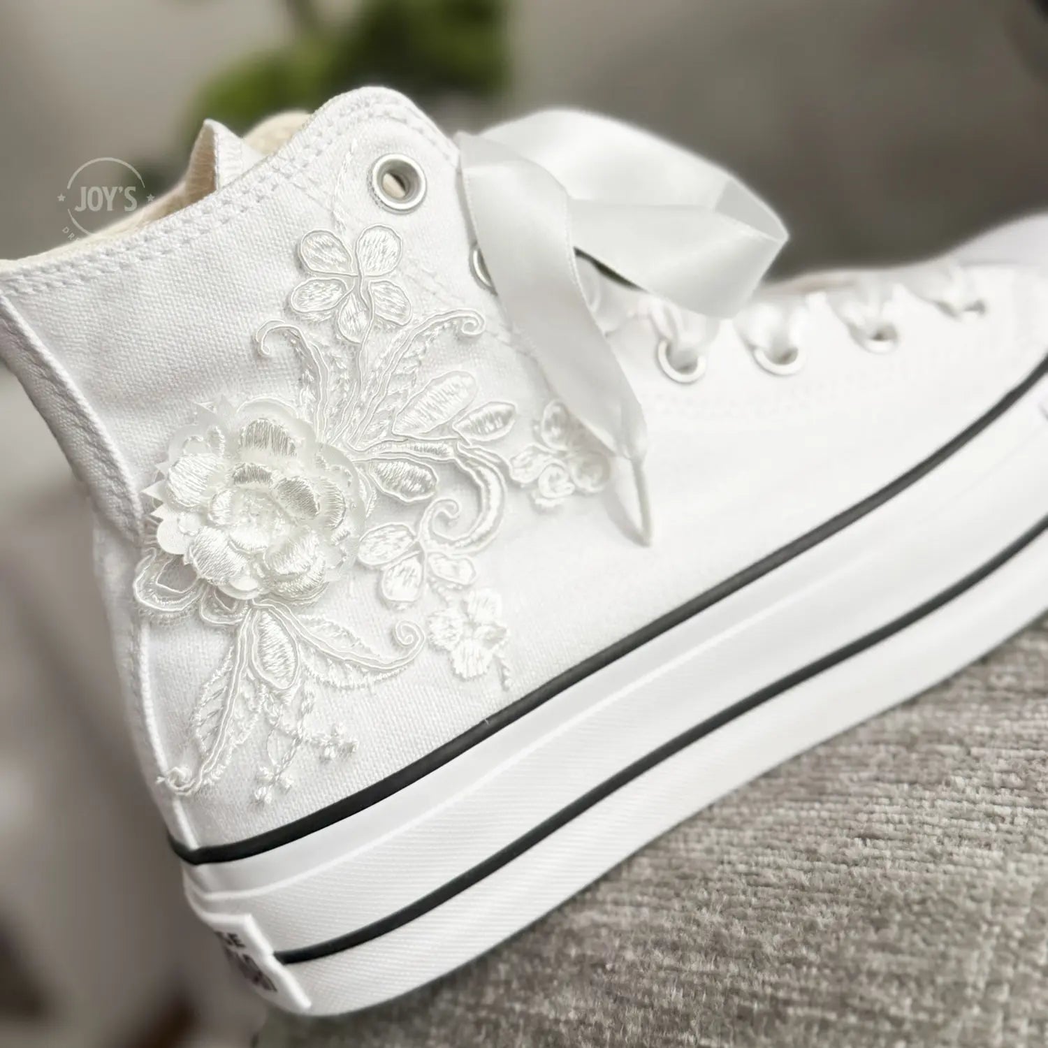 White platform Converse Chuck Taylor wedding sneakers with lace floral appliqués, satin ribbon laces, and personalized initials printed on the side, shown in a clean studio side view