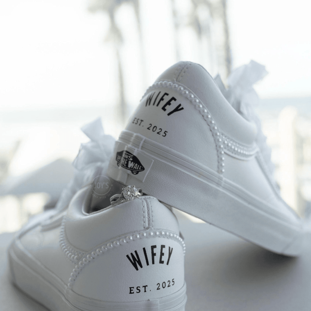 Custom white Vans sneakers with pearl trim and “Wifey EST” lettering on the heel, designed as bridal shoes.