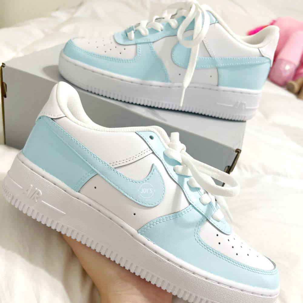Custom Nike Air Force 1 low sneakers with light blue and white color block design, featuring matching blue swoosh and white leather panels.