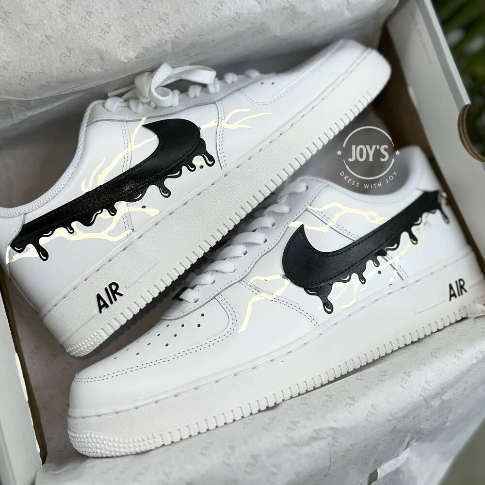 White Nike Air Force 1 with black drip swoosh design and subtle lightning accents, shown inside the shoebox.