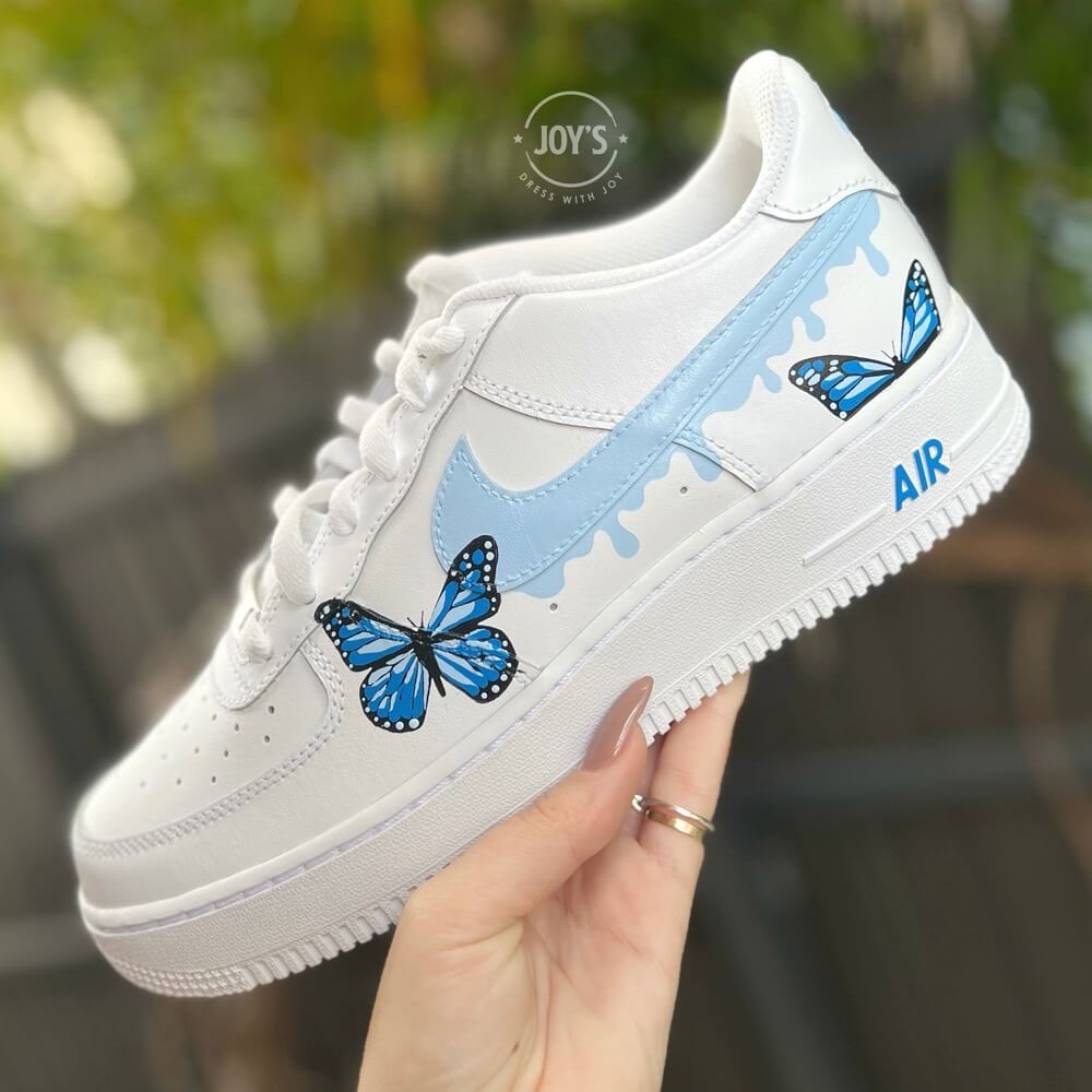 White Nike Air Force 1 Low Sneakers with light blue drip swoosh and hand-painted blue butterfly design.