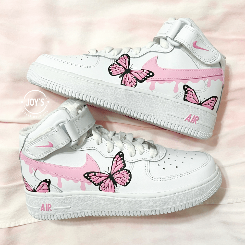 Pair of custom white Nike Air Force 1 sneakers with pink drip swoosh and hand-painted pink butterfly designs, displayed side by side on a soft pink background.