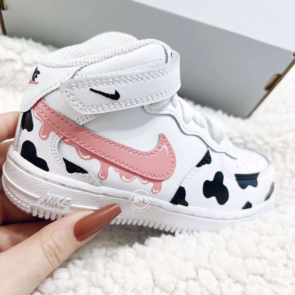 Custom toddler Nike Air Force 1 with black cow-print panels and a pink drip swoosh, white leather base and ankle strap, shown in close-up.