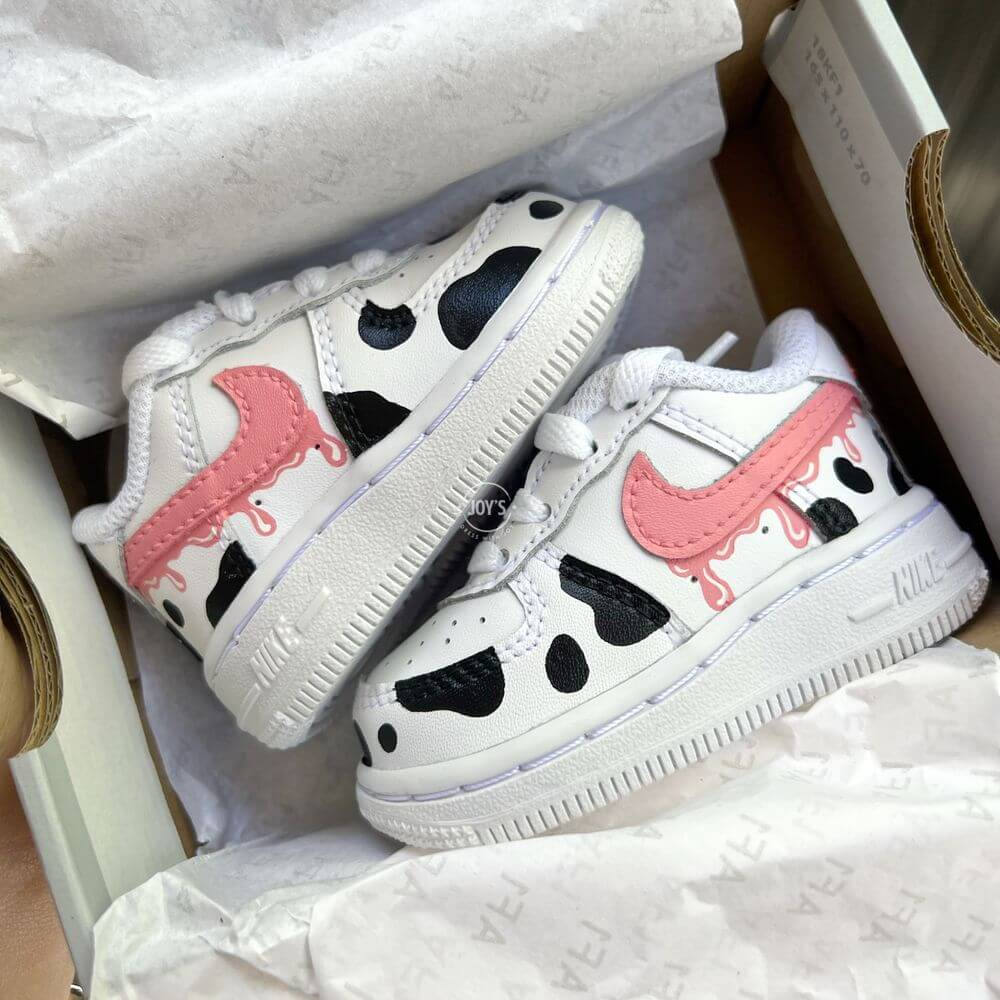 Custom toddler Nike Air Force 1 with black cow-print panels and a pink drip swoosh, white leather base shown in close-up.