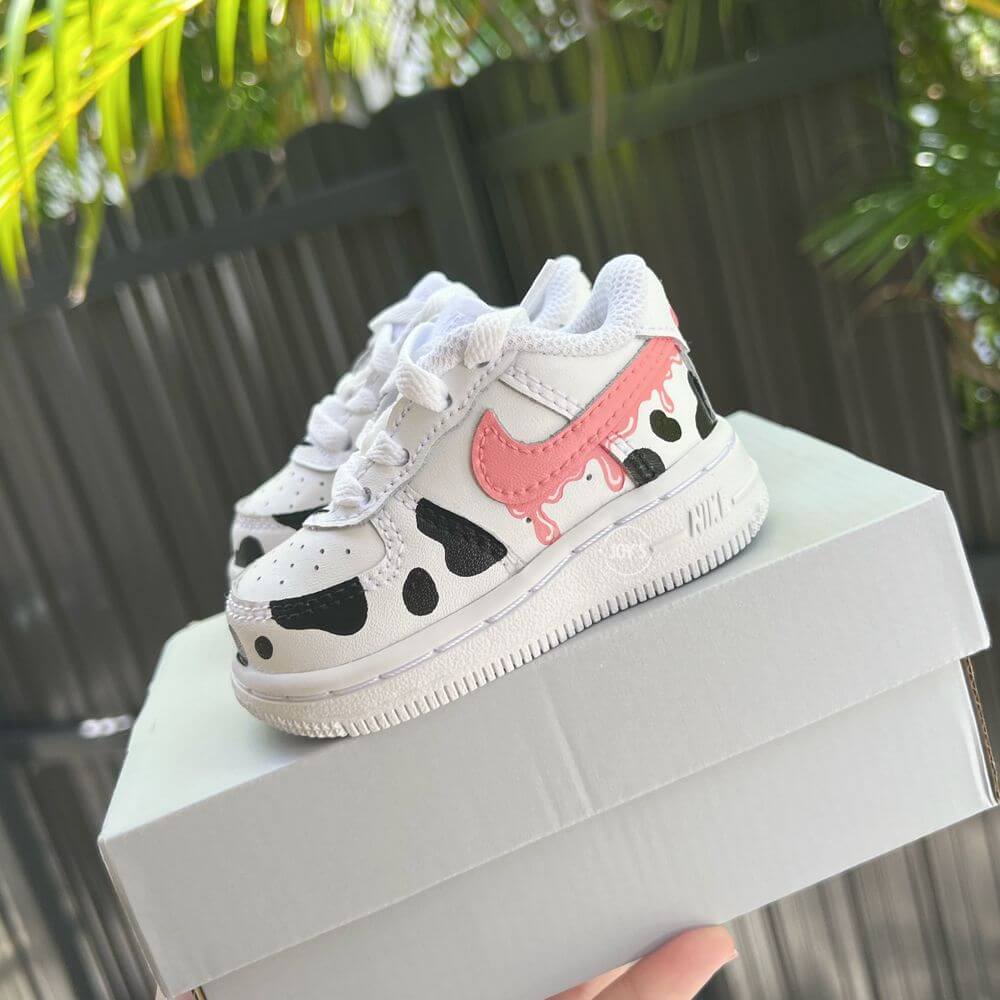 Custom toddler Nike Air Force 1 with black cow-print panels and a pink drip swoosh, white leather base shown in close-up.