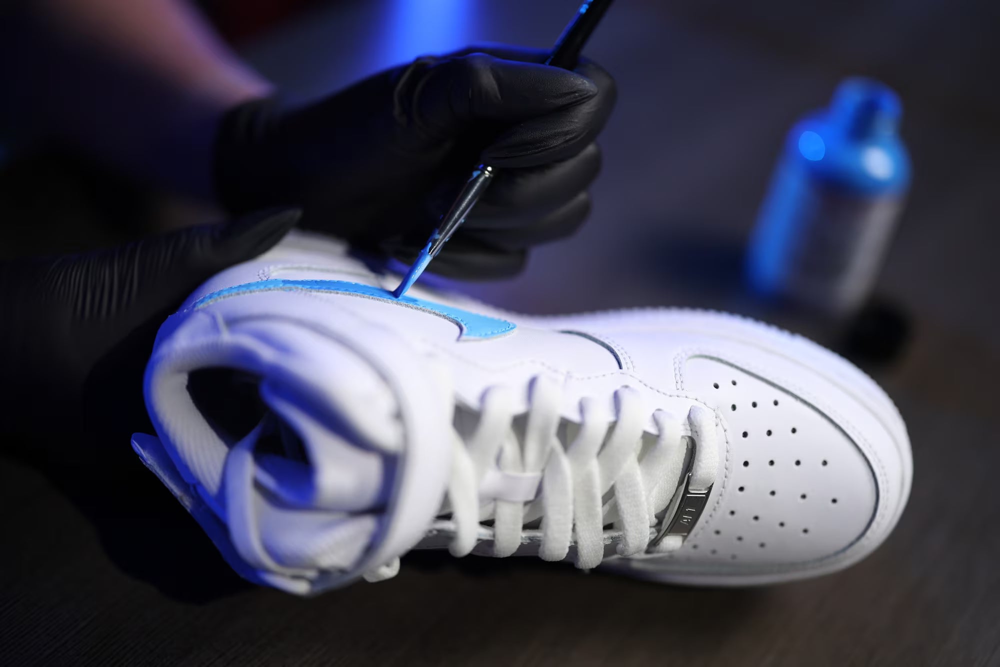White sneaker with blue accents being worked on by a gloved hand.