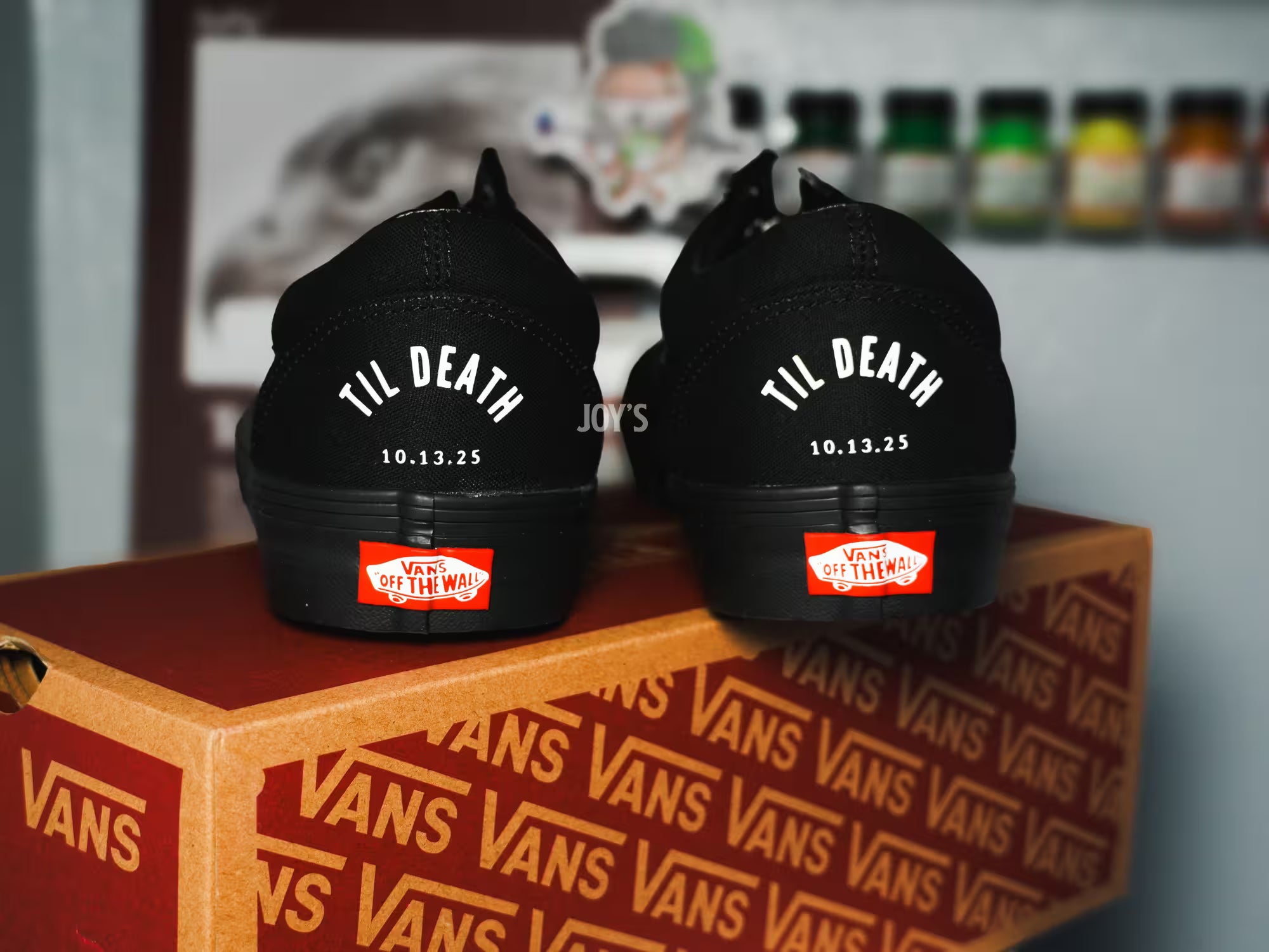 Black Vans custom wedding sneakers with “Til Death” text and wedding date printed on the heels, shown in a rear view on a Vans shoebox