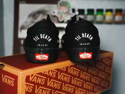 Black Vans custom wedding sneakers with “Til Death” text and wedding date printed on the heels, shown in a rear view on a Vans shoebox