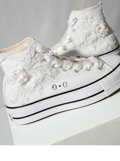 White platform Converse Chuck Taylor wedding sneakers with lace floral appliqués, satin ribbon laces, and personalized initials printed on the side, shown in a clean studio side view