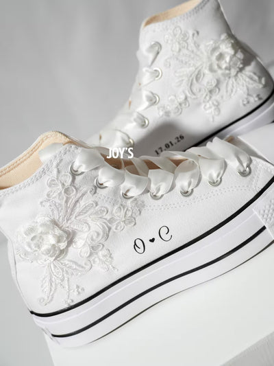 White platform Converse Chuck Taylor wedding sneakers with lace floral appliqués, satin ribbon laces, and personalized initials printed on the side, shown in a clean studio side view
