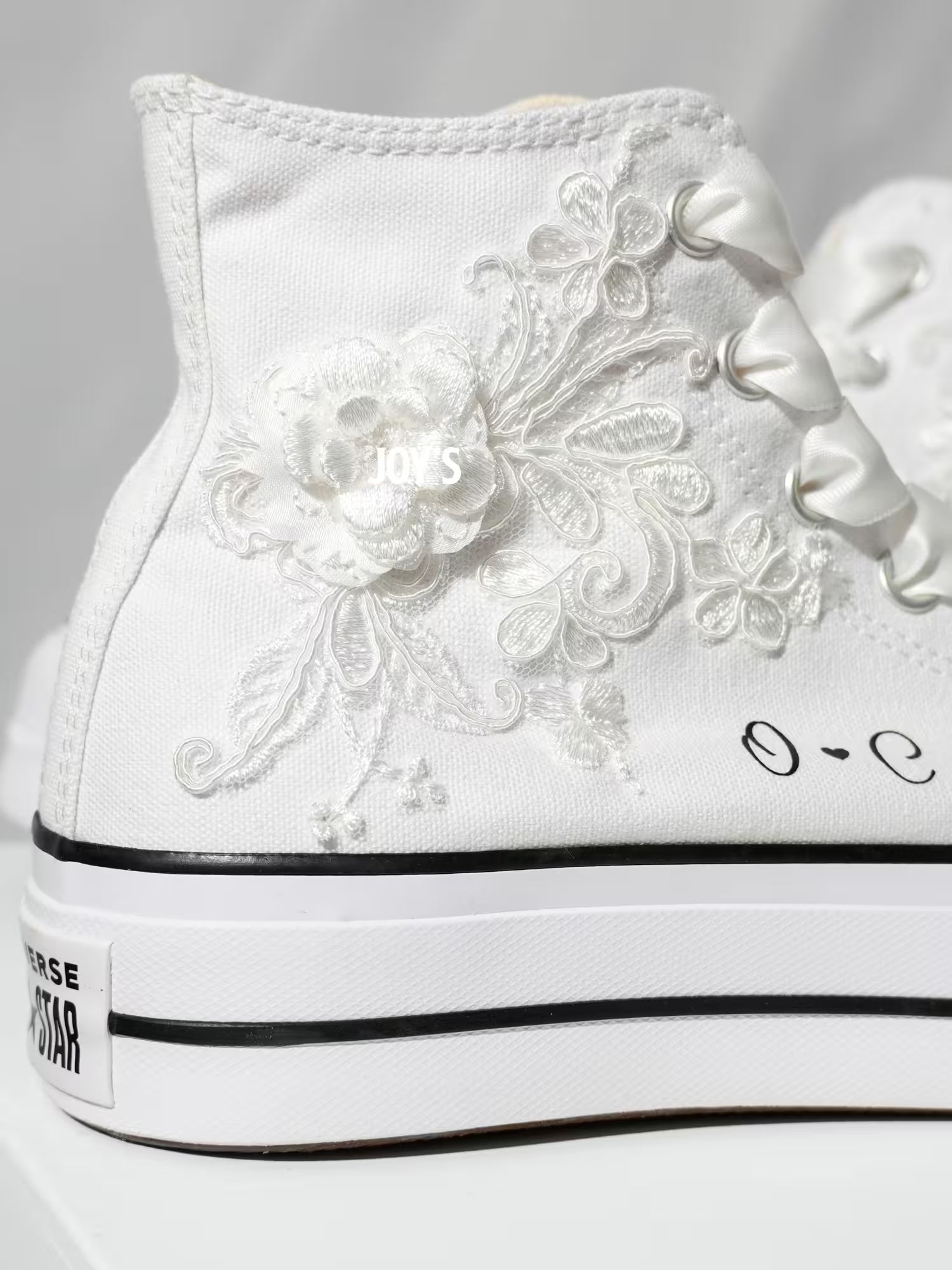 White platform Converse Chuck Taylor wedding sneakers with lace floral appliqués, satin ribbon laces, and personalized initials printed on the side, shown in a clean studio side view
