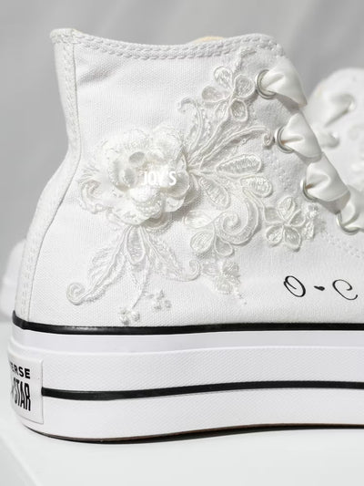 White platform Converse Chuck Taylor wedding sneakers with lace floral appliqués, satin ribbon laces, and personalized initials printed on the side, shown in a clean studio side view
