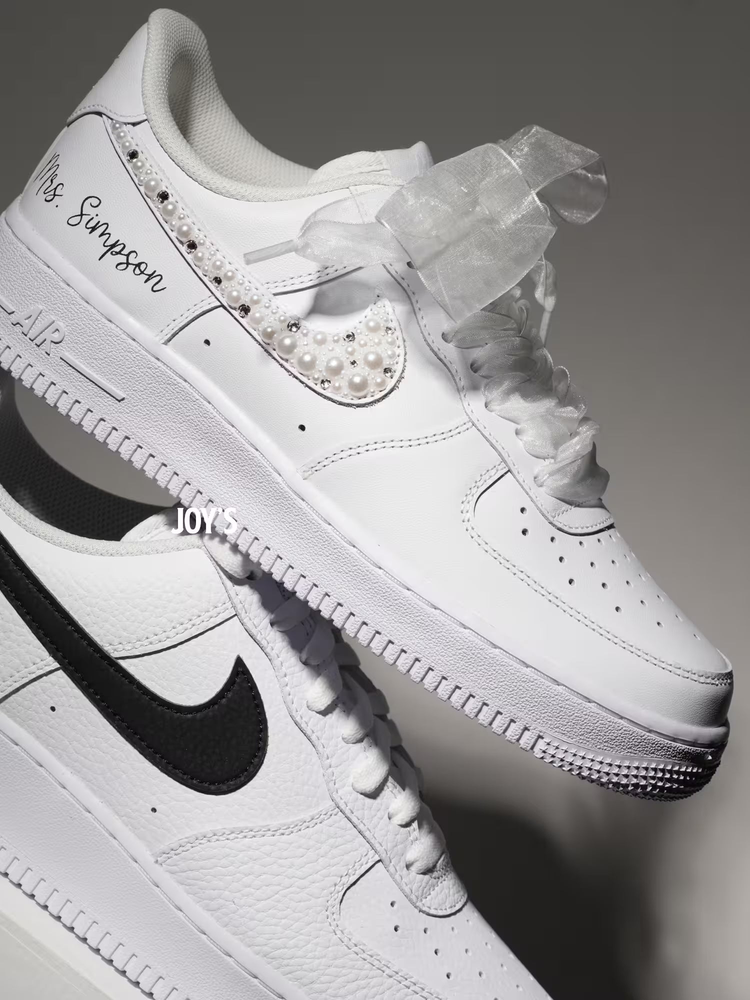 White custom wedding sneakers with pearl and rhinestone embellished swoosh, satin ribbon laces, and personalized last name printed on the side, shown in a close-up detail view