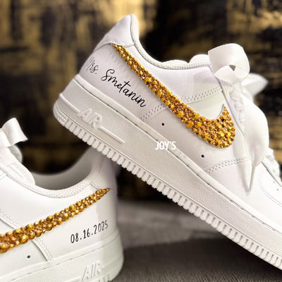 White custom wedding sneakers featuring gold rhinestone swooshes, personalized name and wedding date on the heel, shown in a close-up detail view
