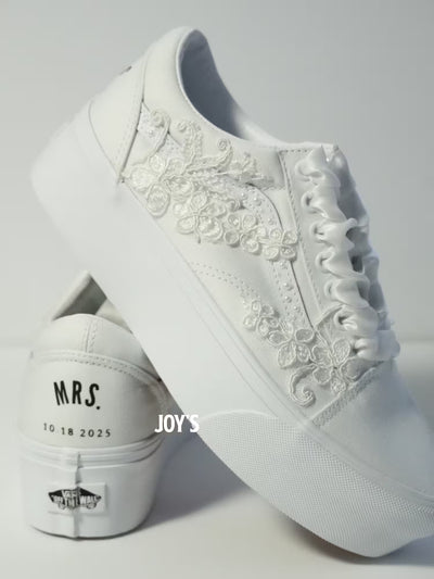 White platform Vans wedding sneakers with lace floral appliqués, pearl detailing, and satin ribbon laces, shown in a close-up side view