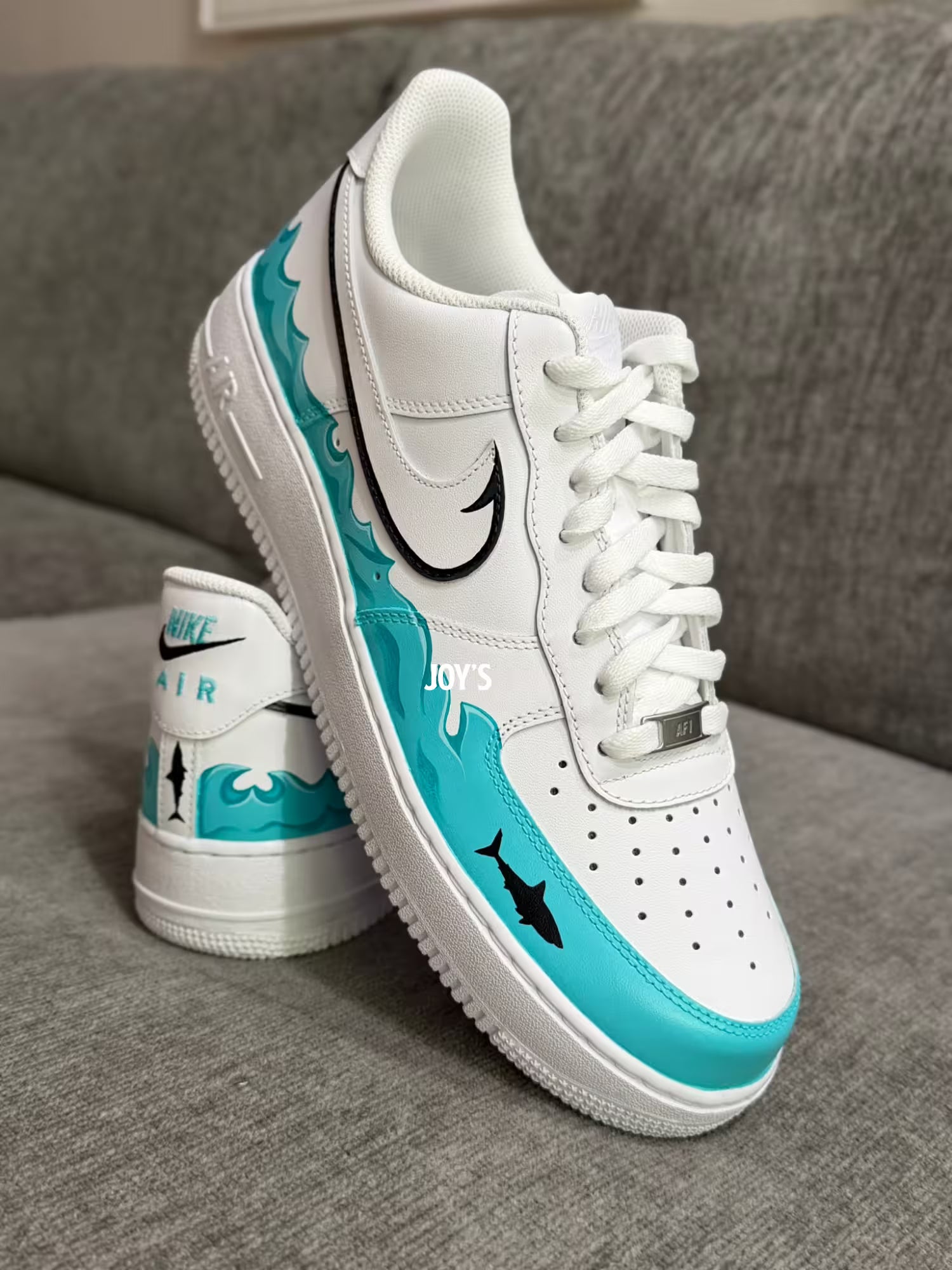 White custom Nike Air Force 1 sneakers with teal sea wave inspired hand-painted details and black swoosh with a shark figure
