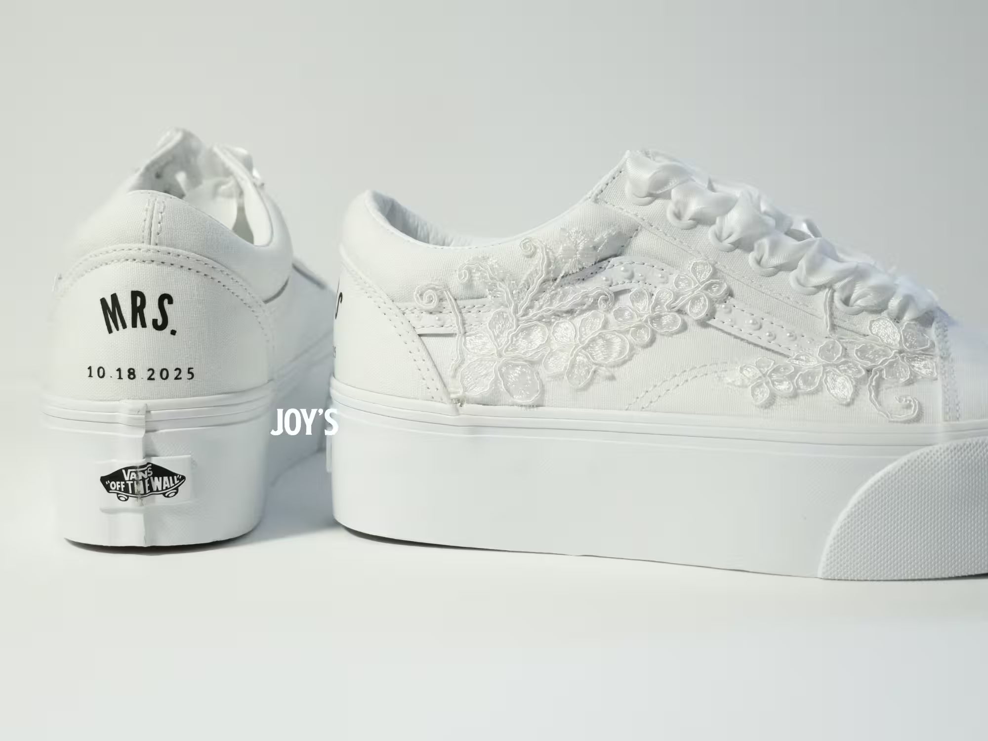 White platform Vans wedding sneakers with lace floral appliqués, pearl detailing, and satin ribbon laces, shown in a close-up side view
