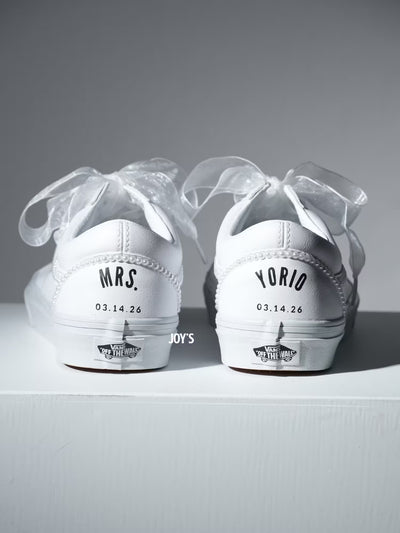 Custom white Vans sneakers with pearl trim and “Mrs.” lettering on the heel, designed as bridal shoes.