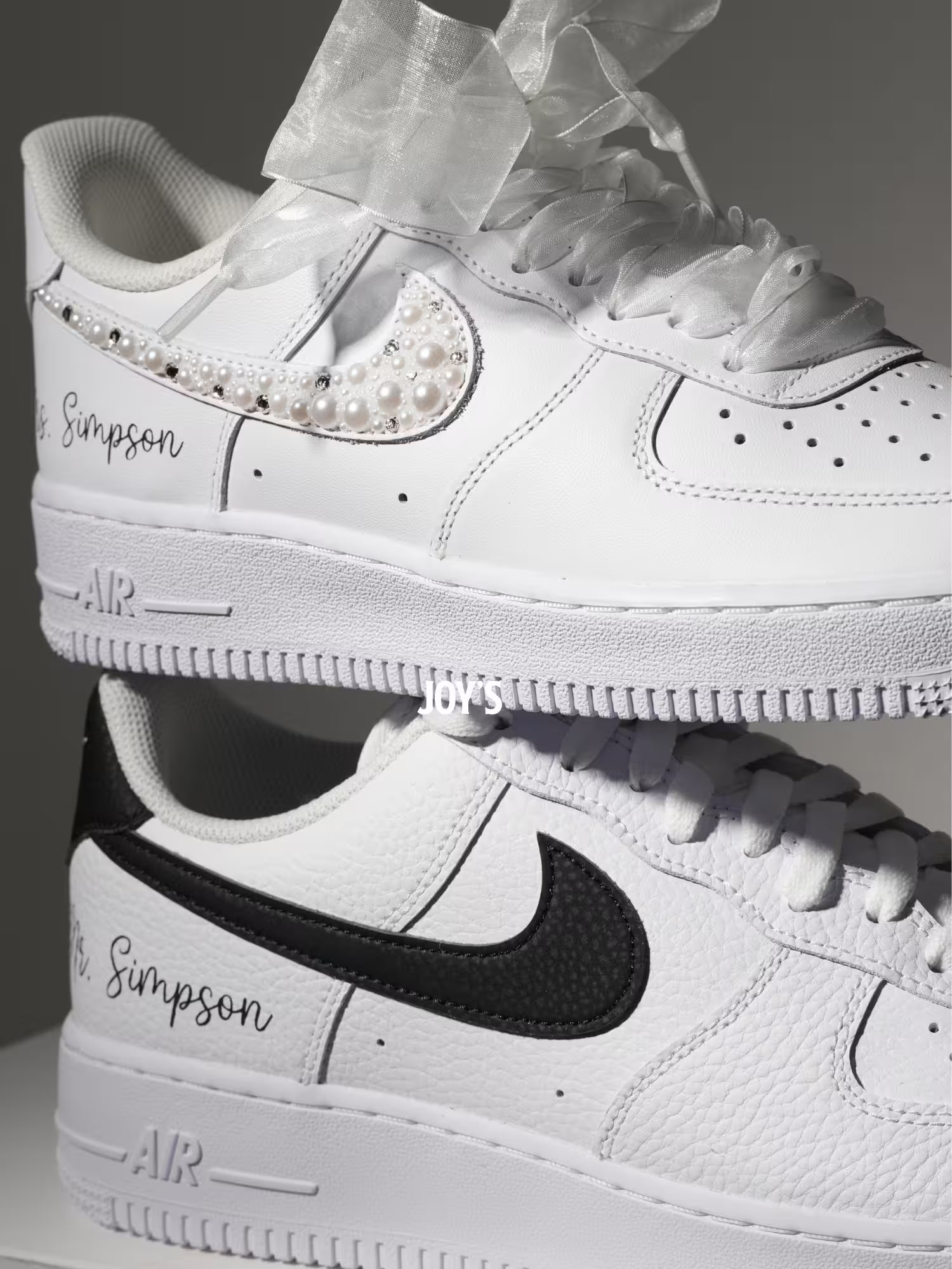 White custom wedding sneakers with pearl and rhinestone embellished swoosh, satin ribbon laces, and personalized last name printed on the side, shown in a close-up detail view
