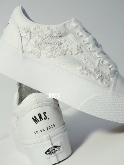 White platform Vans wedding sneakers with lace floral appliqués, pearl detailing, and satin ribbon laces, shown in a close-up side view